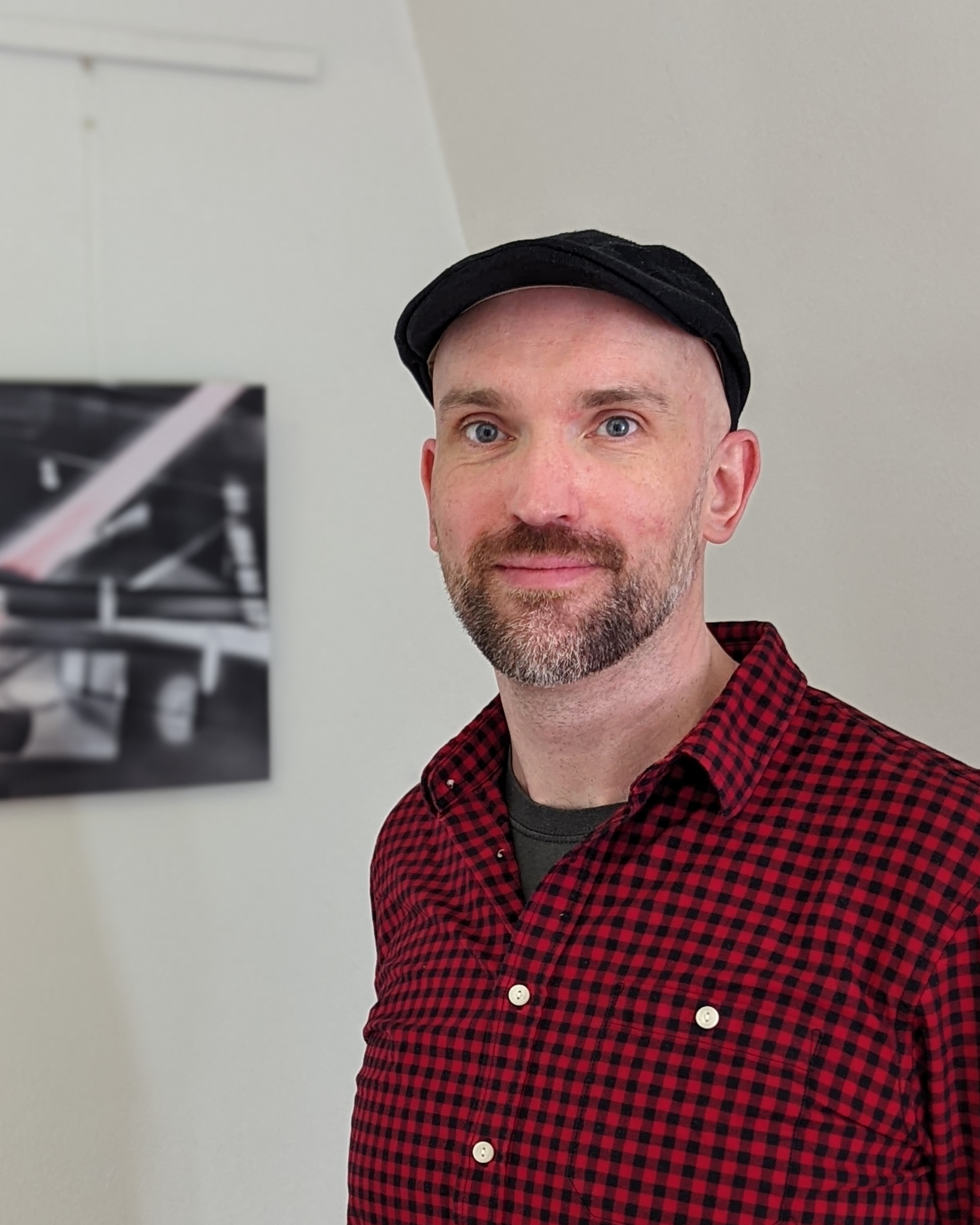 Portrait of the artist Björn Berg. He have an open friendly face. One of his abstract pictures is visible in the background.