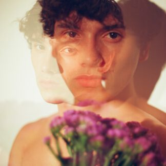 Analog color photograph of a bare male torso holding purple flowers, exploring masculinity, tenderness, desire and vulnerability.